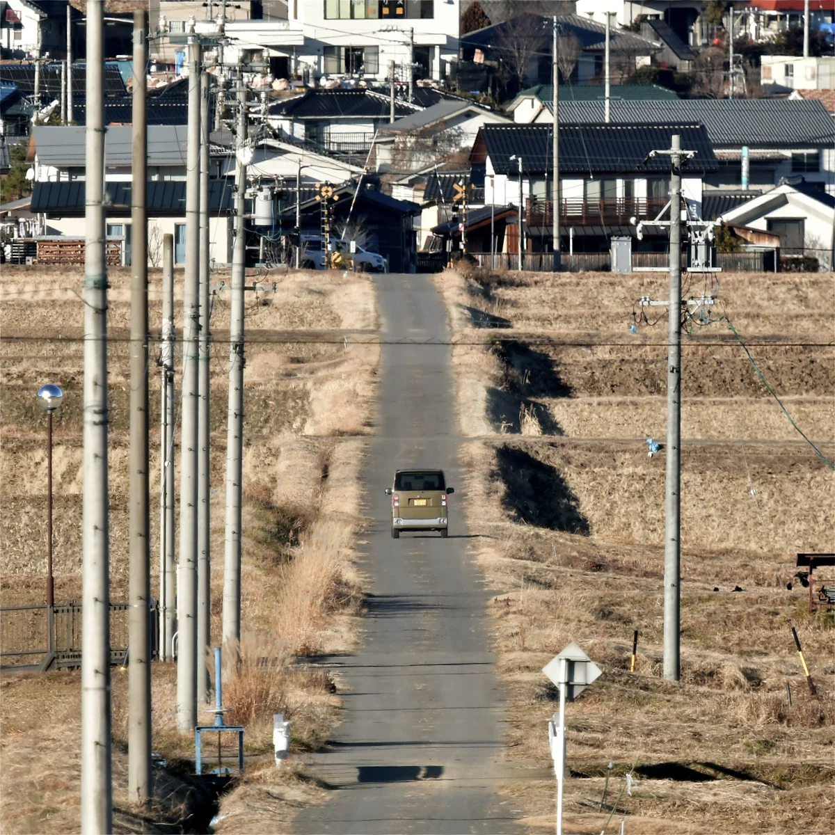 農道を車が走っている その先に踏切が見える