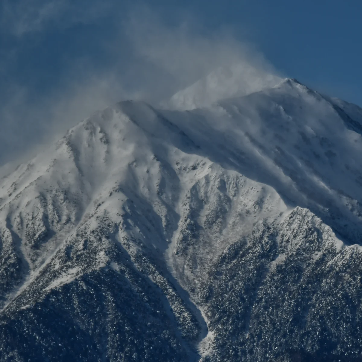 山の稜線から雪煙が流れている