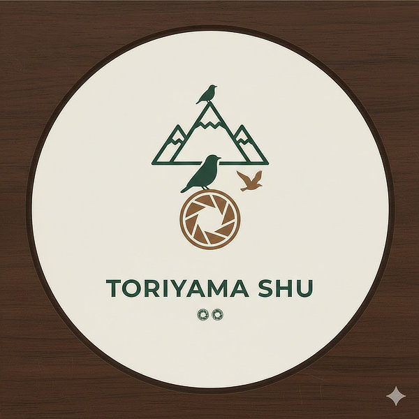 円形の白い背景に上部には深緑色のラインで描かれた三つの山の稜線、頂上に小さな鳥のシルエット。下に茶色のカメラの絞りを模した円形の図形、その上に一羽の鳥、右側には羽ばたく鳥が配置されているロゴ。全体的に落ち着いたアースカラーで構成されミニマルなデザイン。